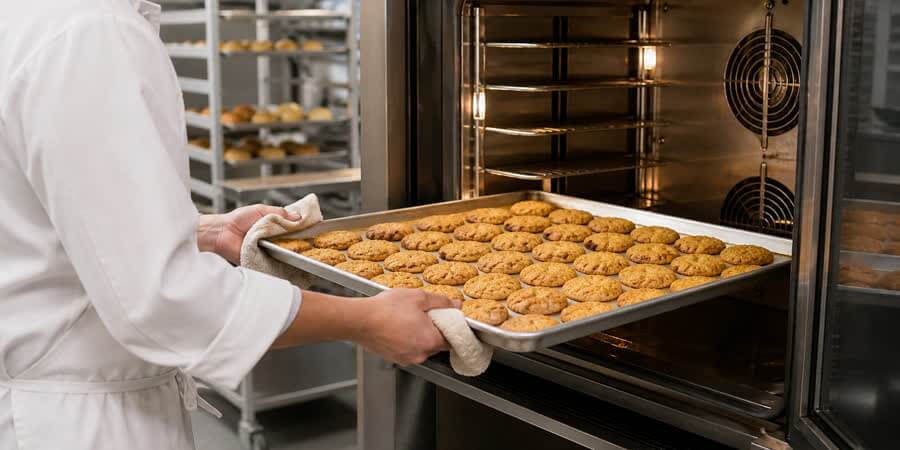 Baker loading a full-size sheet pan of cookies into a commercial oven