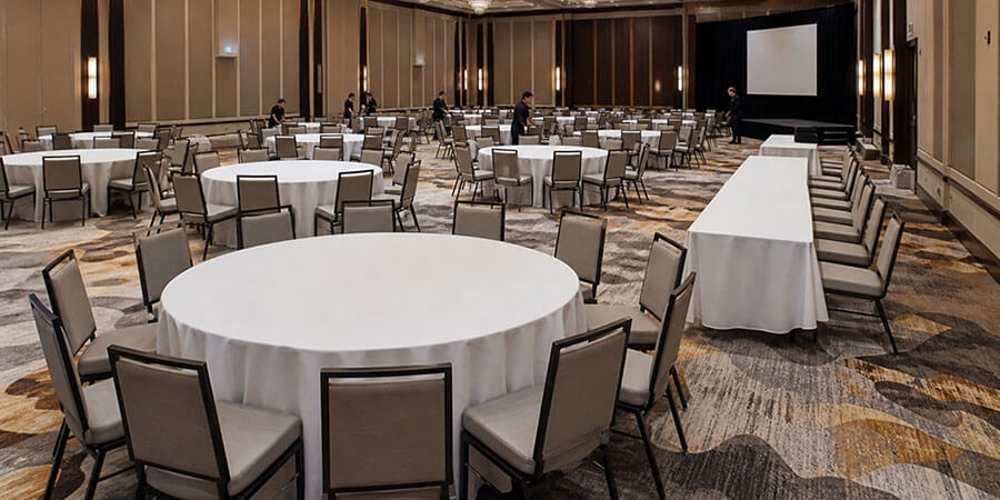 Banquet hall being set with 60-inch round tables for eight and a row of rectangular folding tables