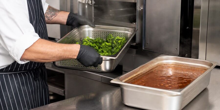 Chef lifting a perforated hotel pan of steamed vegetables from a steamer