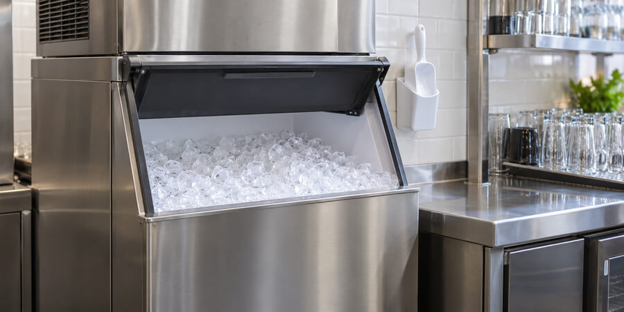 Commercial ice machine with an open bin of ice and a scoop stored in an exterior holder.